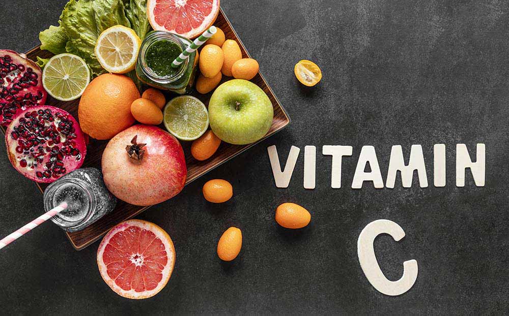 Разные овощи и фрукты и надпись Vitamin C латинскими буквами на черной поверхности. Вид сверху